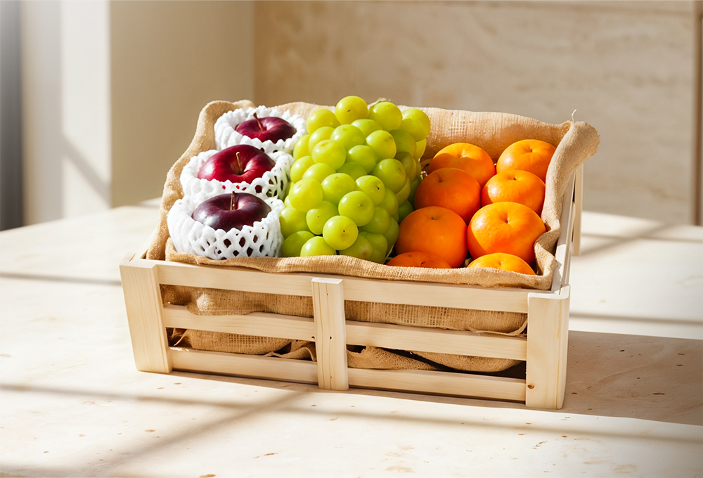 A wooden fruit box filled with fresh green grapes, red apples, and bright mandarins, neatly arranged on burlap in warm natural sunlight.