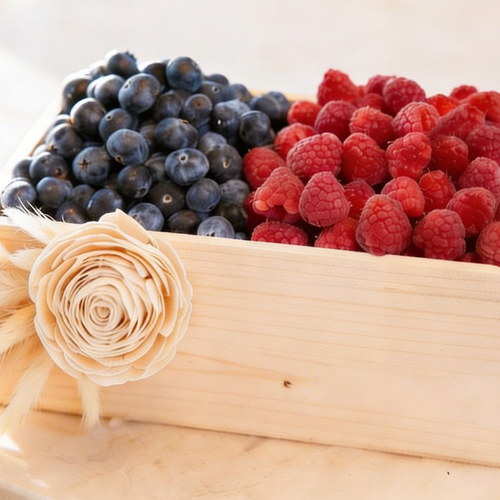 A beautifully arranged **fruit box** filled with fresh blueberries and raspberries, accented with a decorative flower in soft natural light.
