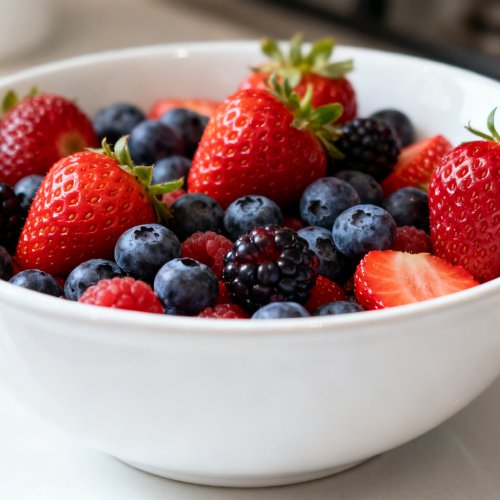 This image shows a bowl filled with a colorful assortment of fresh berries, including strawberries, blueberries, and blackberries, placed on a light countertop.