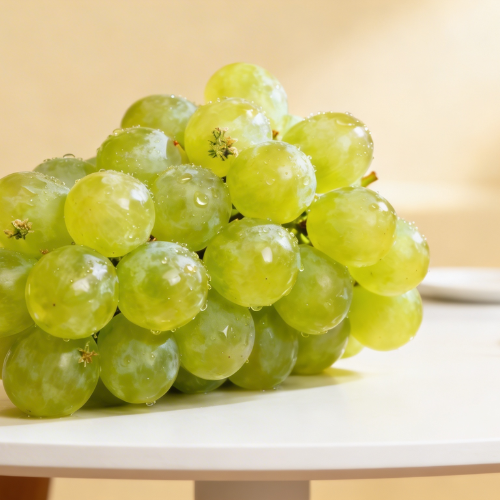 A fresh bunch of glossy green grapes with water droplets, beautifully lit to highlight their juicy and vibrant appearance.