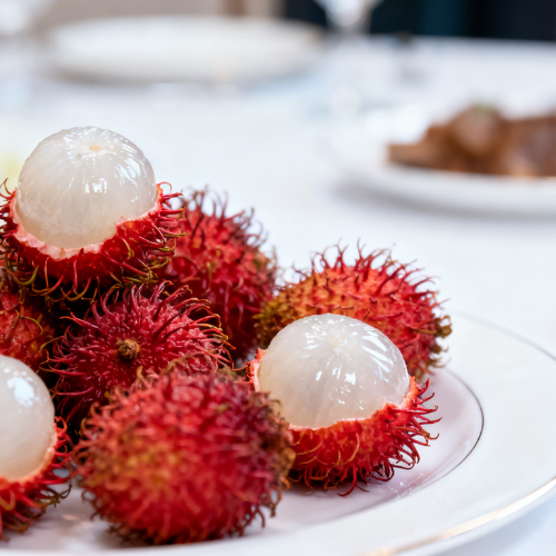 Fresh rambutans with spiky red skin, some peeled to reveal their juicy translucent white flesh on a plate.